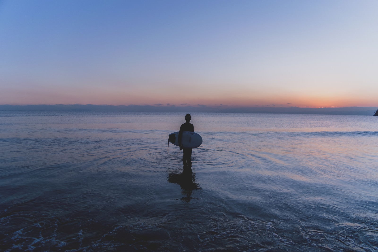 「日没の海に佇むサーファーの男性」の写真