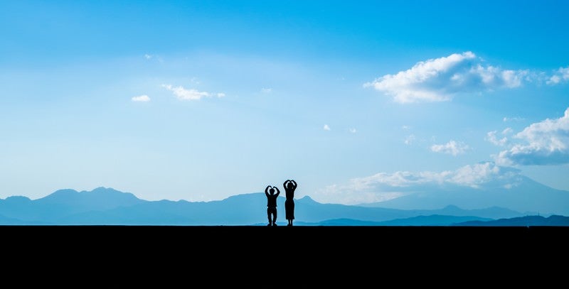 堤防の上でウッキーポーズをとる恋人（シルエット）の写真