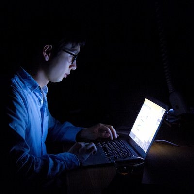 暗闇でPCを使う残業中の男性の写真