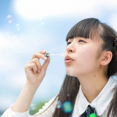 空に向かってシャボン玉を吹くツインテールの女の子の写真