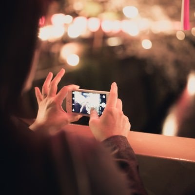 スマホで夜桜を撮影する女性の写真