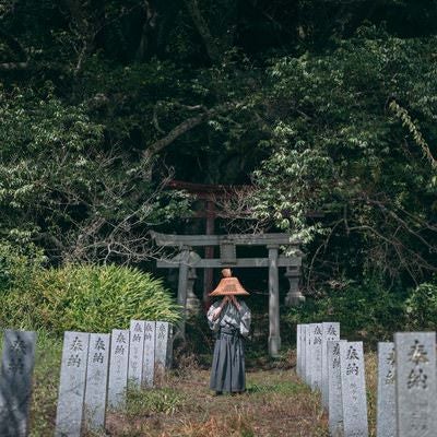 鳥居の前に佇む笠を深く被った侍の写真