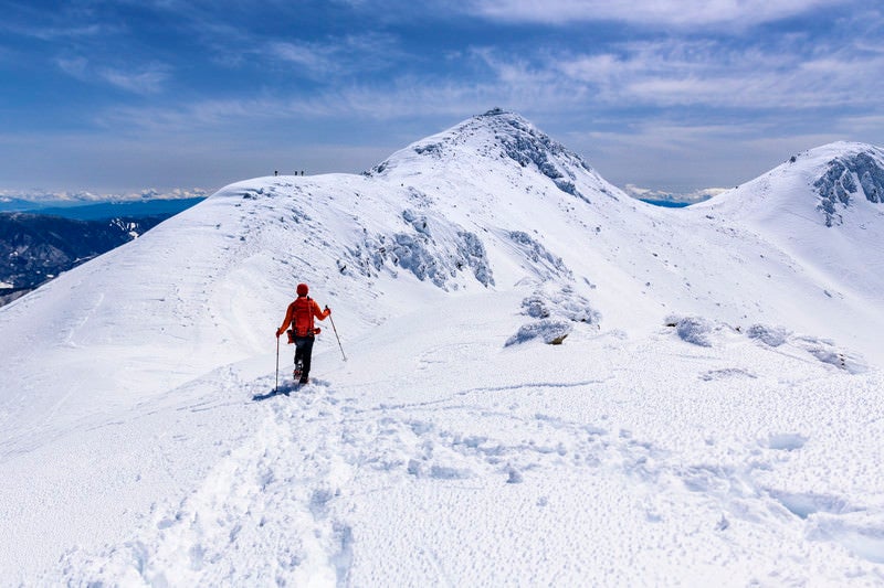 冬の乗鞍岳を登る赤い登山者の写真