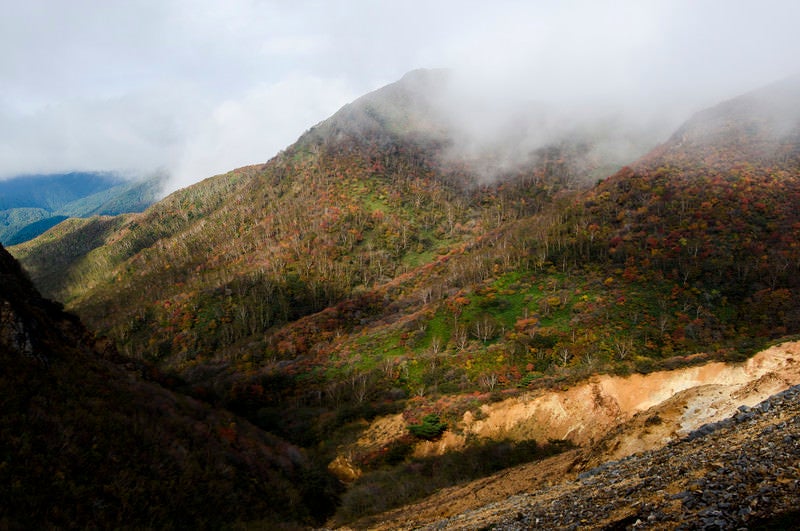 雲の隙間から紅葉をのぞかせる那須岳（なすだけ）の写真