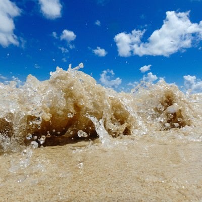 砂浜に打ち上げるさざ波と水しぶきの写真