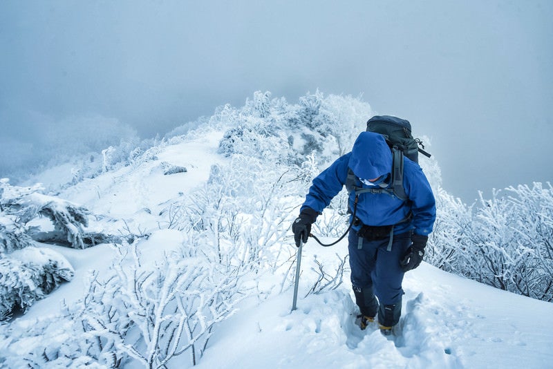 雪深い登山道で山頂を目指す登山者の写真