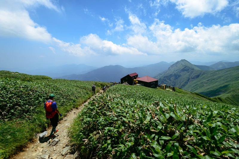 谷川の尾根を歩き山小屋を目指す登山者達の写真