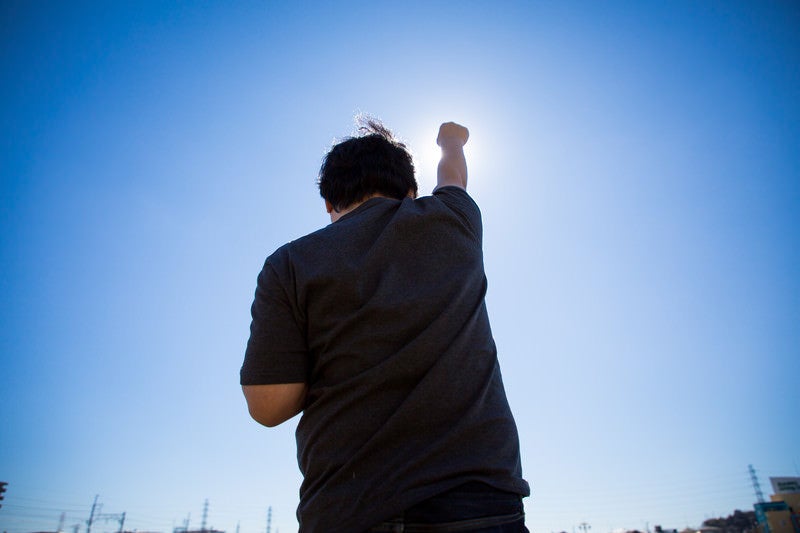 太陽に向かって拳を高々とあげる後ろ姿の写真