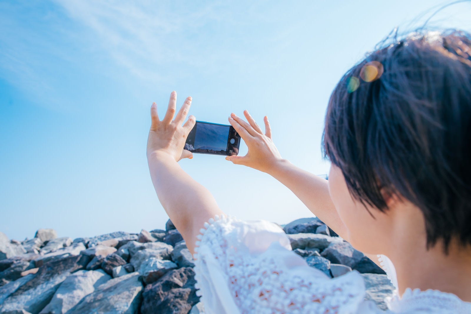 「スマホで青空を撮影する女性」の写真［モデル：にゃるる］