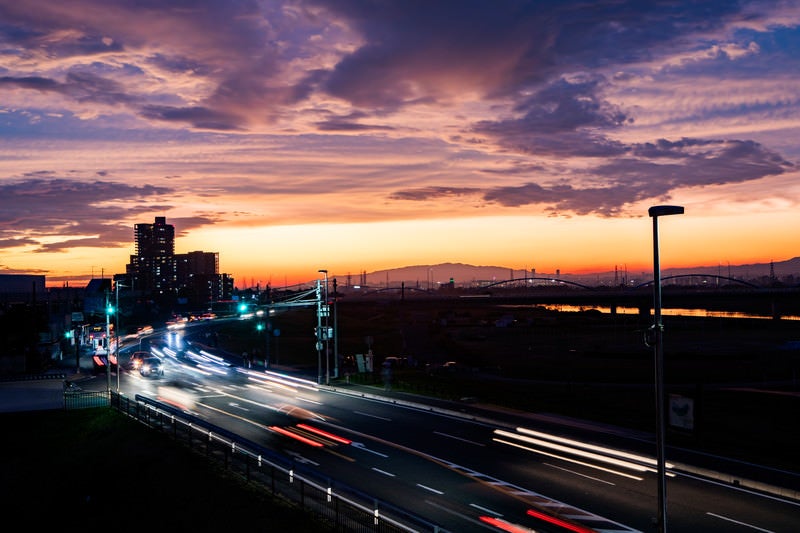 夕焼けの空と車道に残る光跡の写真