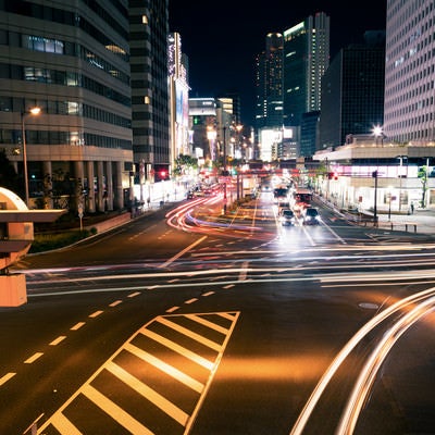 夜の交差点を行き交う車の光跡の写真