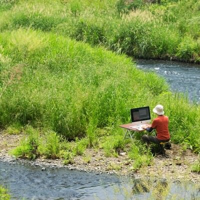 川のせせらぎを求めて下流の中洲で作業をするノマドワーカーの写真