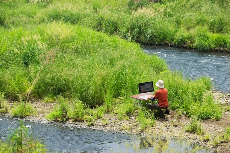 川のせせらぎを求めて下流の中洲で作業をするノマドワーカーの写真