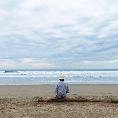 流木の上に座りサーファー達を見つめるエンジニアの写真