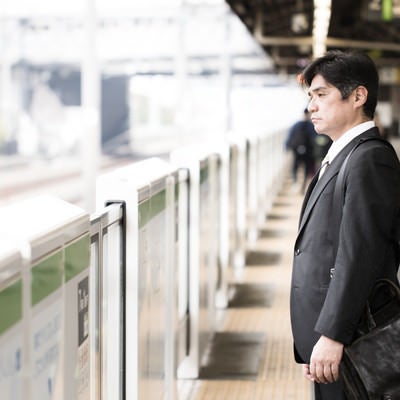 駅のホームで険しい表情の中年会社員の写真