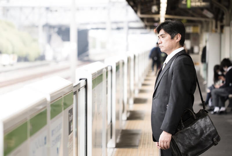 駅のホームで険しい表情の中年会社員の写真