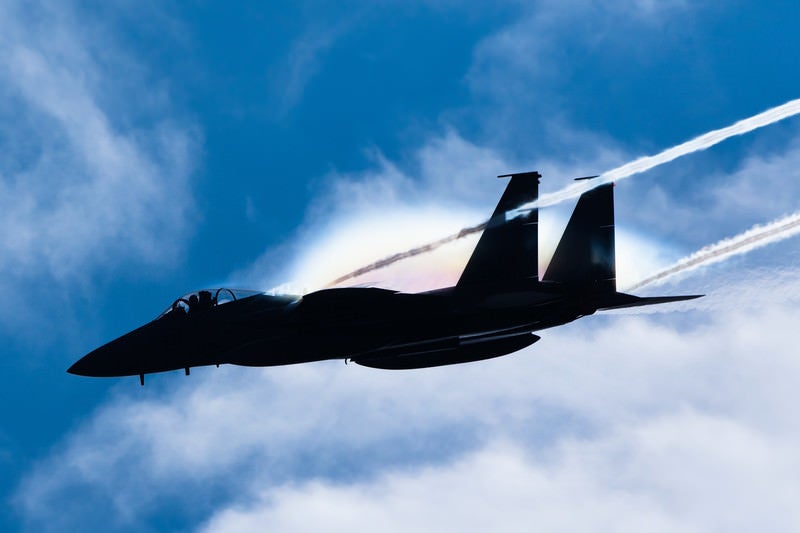 虹を纏って進む戦闘機のシルエット（F-15）の写真