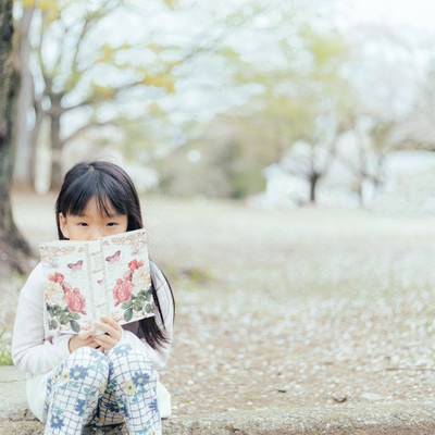 公園で洋書を読む女の子の写真