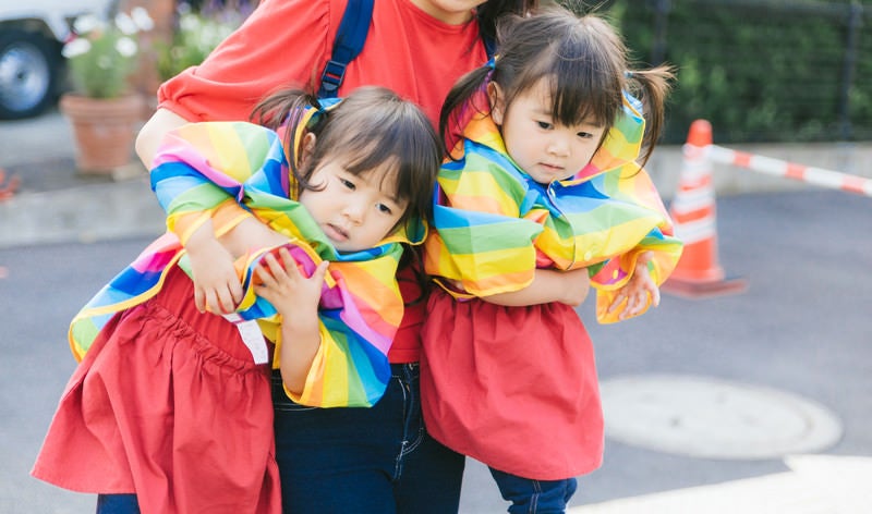 駄々をこねる双子と抱きかかえる母親の写真