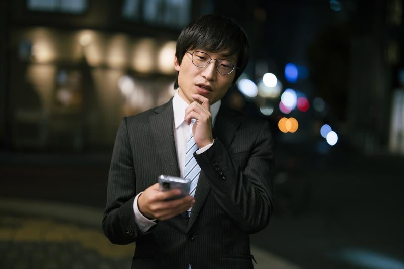 屋外でスマートフォンをチェックする男性の写真