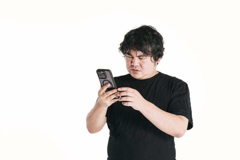 悩みながらスマートフォンを眺める男性の写真