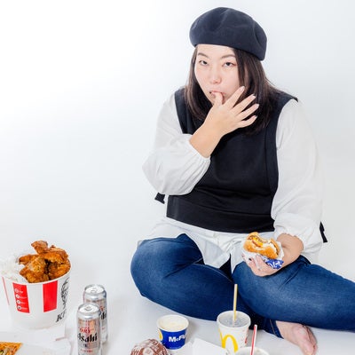 指を舐めるジャンクフードを食す女性の写真