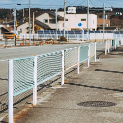 小高のフェンスがある歩道と街並みの写真