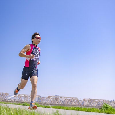 よく晴れた日にトレーニングで河川敷をランニングするトライアスロンの選手の写真