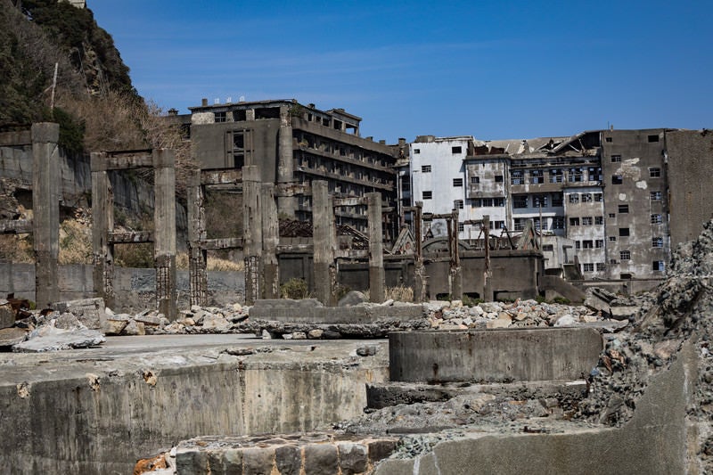 貯炭場越しの端島保育園跡と70号棟小中学校跡（軍艦島）の写真