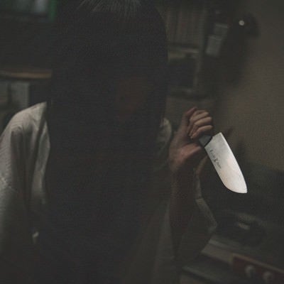 暗がりで包丁を持つ黒髪の女性の写真