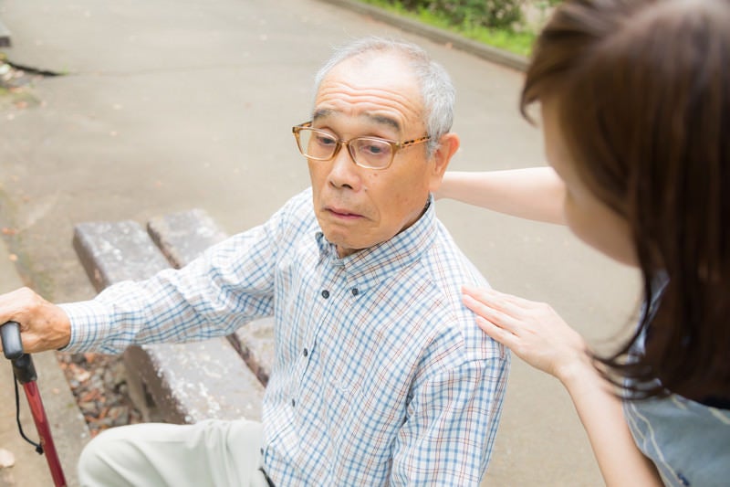 疲れてベンチに座る老人に声をかける女性の写真