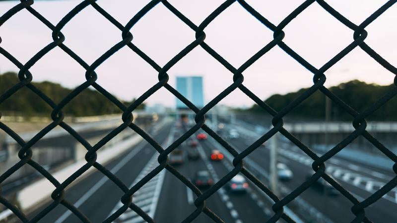 フェンス越しに見る都市と高速道路を走行する車の写真