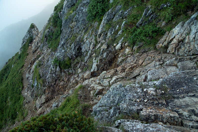 崖沿いを進む登山道の写真