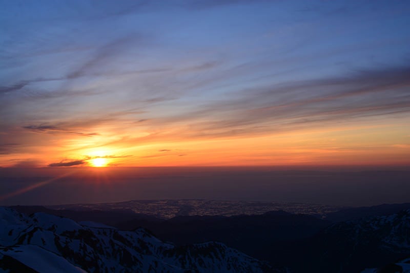 残雪の山から見る日本海に沈む夕日の写真