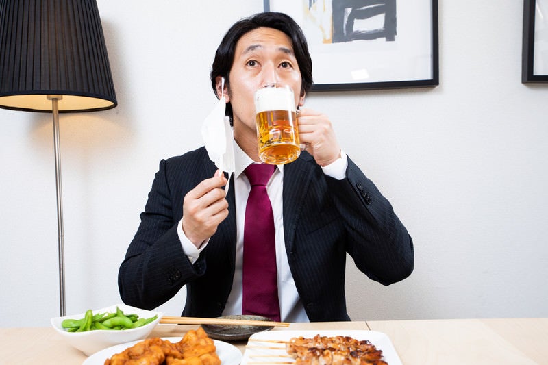 マスクをずらして生ビールを飲む会社員の写真