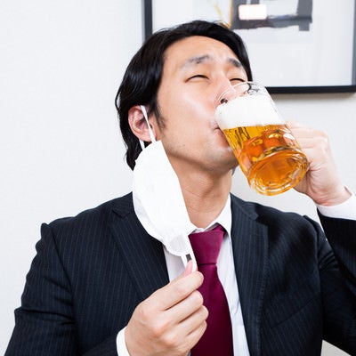 マスクを外して生ビールを飲むサラリーマンの写真