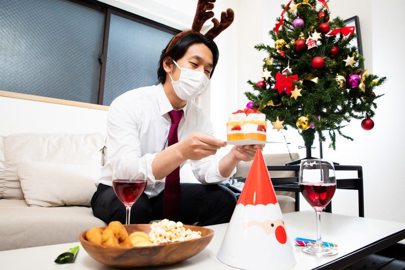 クリスマスケーキを見つめるマスク着用の会社員の写真