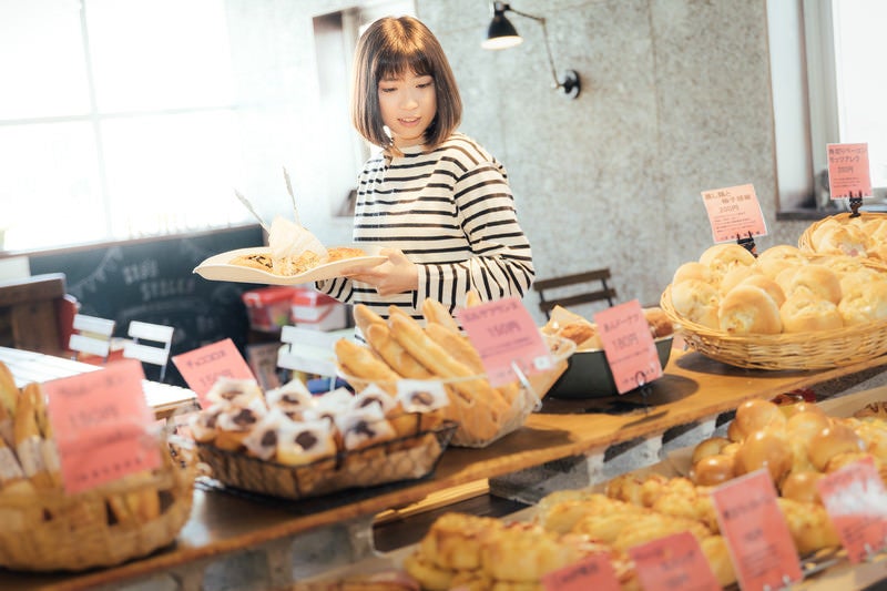 手作りパンのお店でトレイを手に取り店内を歩く女性の写真