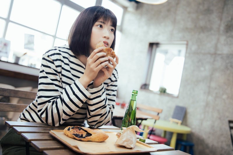 フードコートでおやつに菓子パンを食べる女性の写真