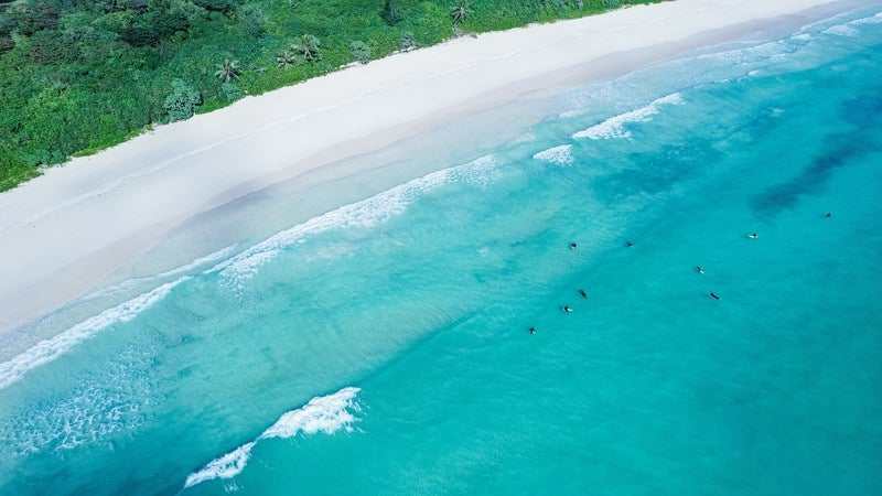 白浜に寄せる波と波待ちするサーファーの写真