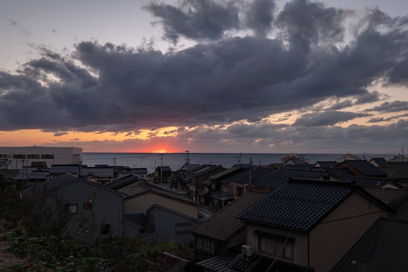 沈む夕日と海沿いの民家の写真