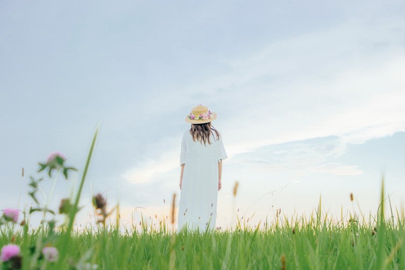 草原で立ちつくす麦わら帽子の女性の写真