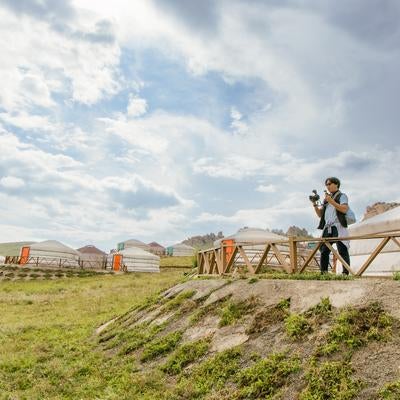 草原に広がるゲルの風景をカメラに収める旅人の写真