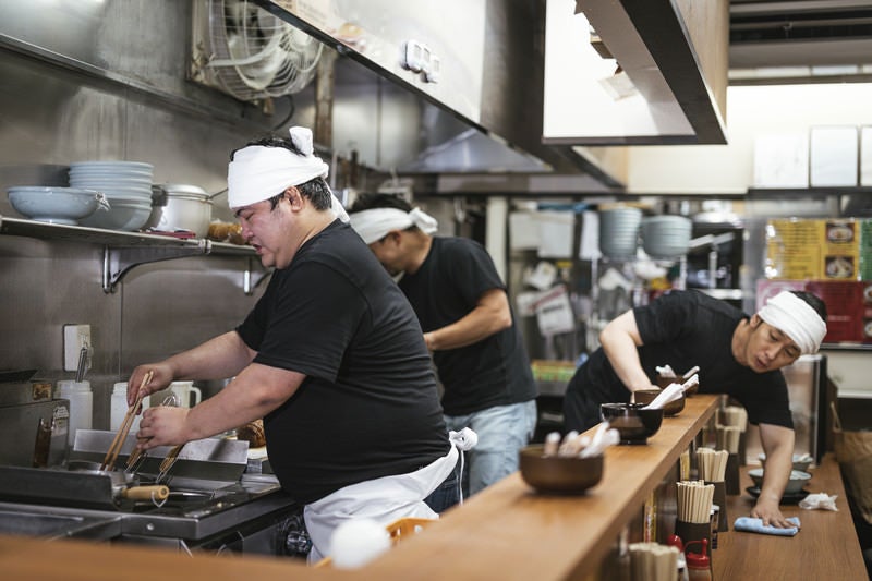 ピークタイムが落ち着いてきたラーメン屋の店内と厨房の写真