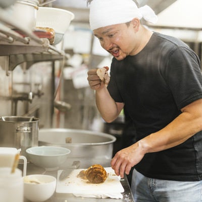 チャーシューをつまみ食いする外国人の店員の写真