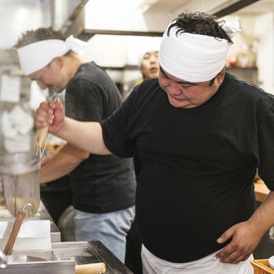 力強く湯切りするラーメン店主の男性の写真