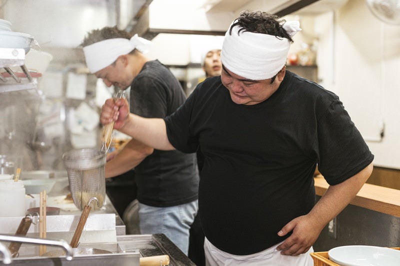 力強く湯切りするラーメン店主の男性の写真