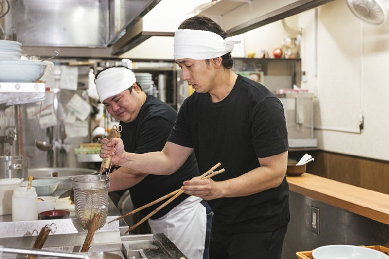 湯切りにチャレンジする新人店員の写真