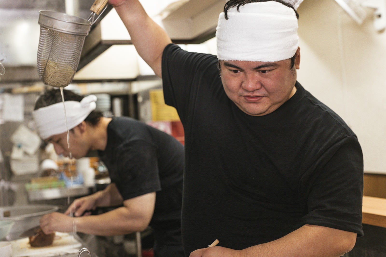 「湯切り中に考え事をして止まる店主」の写真［モデル：段田隼人 大川竜弥］