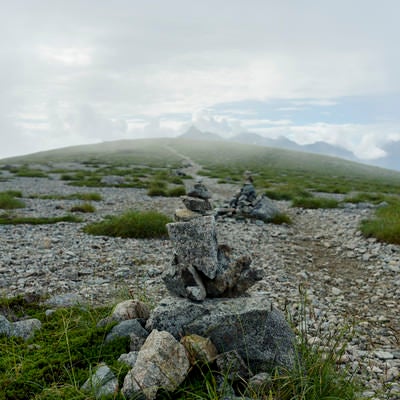 積み上げられたケルンとガスの向こうの槍ヶ岳（鷲羽岳）の写真